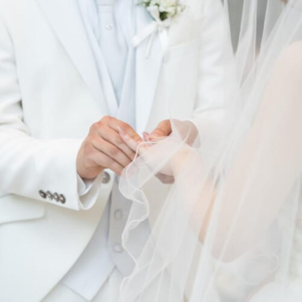 永遠の愛を誓う指輪交換の瞬間。新郎様の純白のタキシードと、ヴェール越しの新婦様の手元が美しい、軽井沢での感動的なセレモニー。