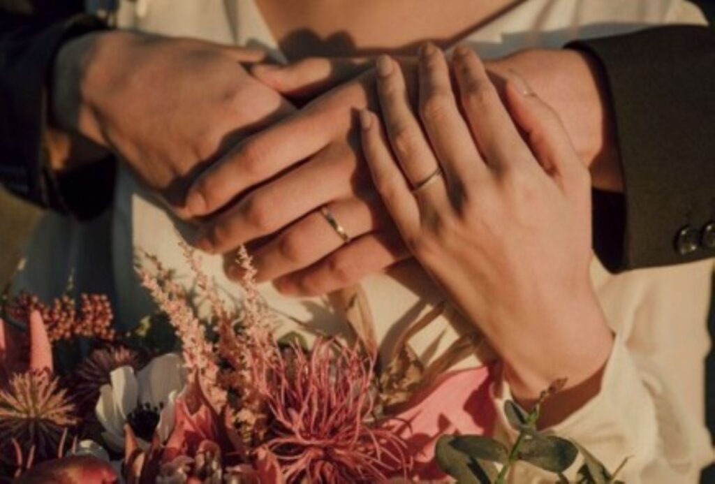 愛の証である結婚指輪が薬指に輝く。そっと重ねた手は、お二人の固い絆と信頼を象徴しています。ブーケが彩る、温かくロマンチックなワンシーンです。