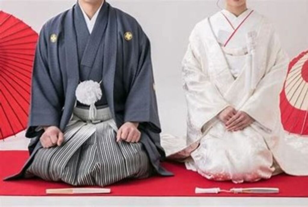 紋付袴と色打掛の和装姿で、可愛らしいハートのポーズ。緑が望める和室での前撮りは、伝統的な美しさとモダンな遊び心を両立できます。幸せあふれる一枚。