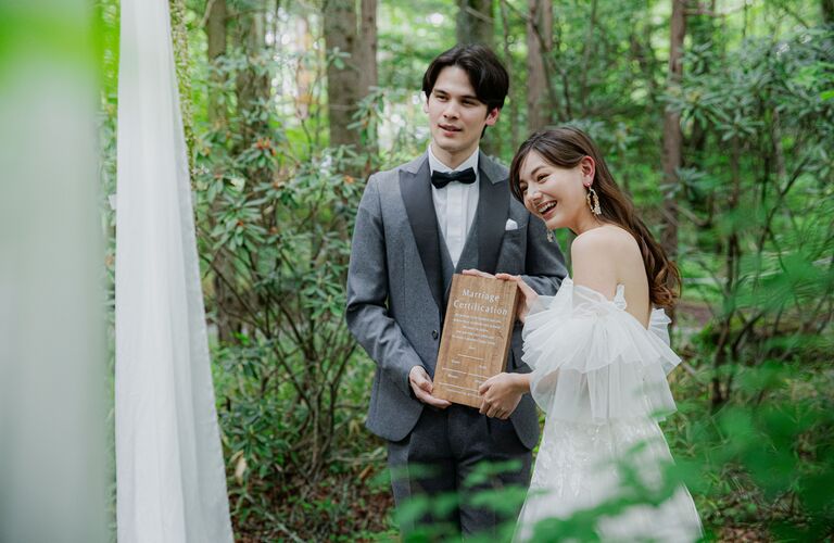 軽井沢リゾートウェディングにぴったりの、木製結婚証明書を持つ新郎新婦。アネーリ軽井沢の森の木漏れ日の中で撮影した、おしゃれなロケーションフォト。