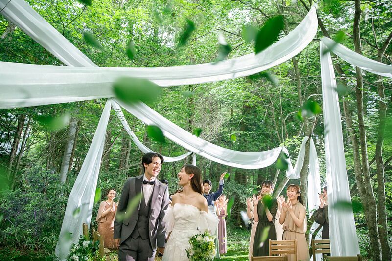 軽井沢の新緑の森で叶えるガーデン挙式。降り注ぐ自然光と緑のシャワーの中を歩く新郎新婦。開放的でナチュラルなリゾートウェディングのシーン。
