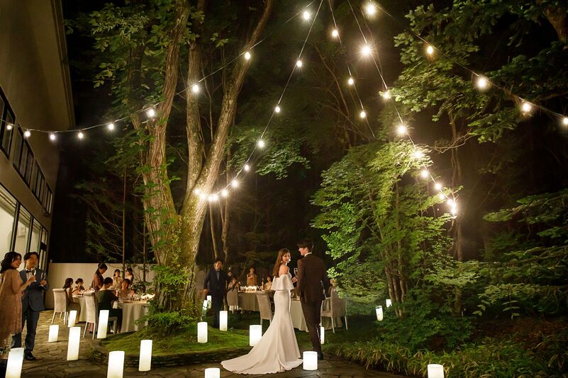 アネーリ軽井沢のナイトウェディング。森の中のガーデンで、電飾とキャンドルに囲まれ歓談するゲスト。軽井沢で叶えるリゾート婚の幻想的な夜のガーデンパーティ。