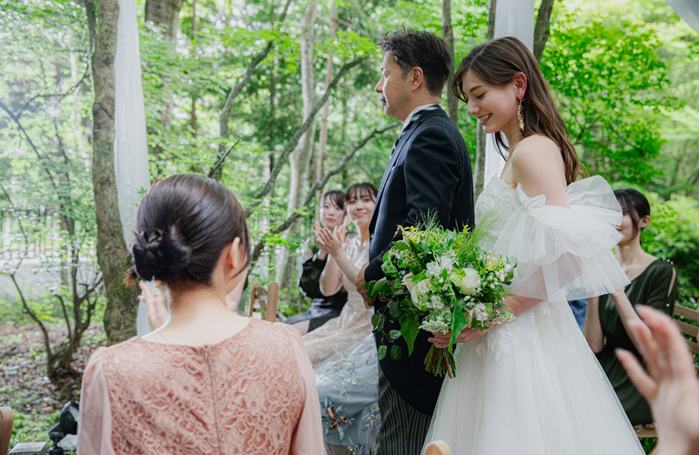 軽井沢リゾートウェディング。純白のウェディングドレスとグリーンブーケを持つ新婦。ゲストの拍手が響くアネーリ軽井沢の森の結婚式の感動的な瞬間。