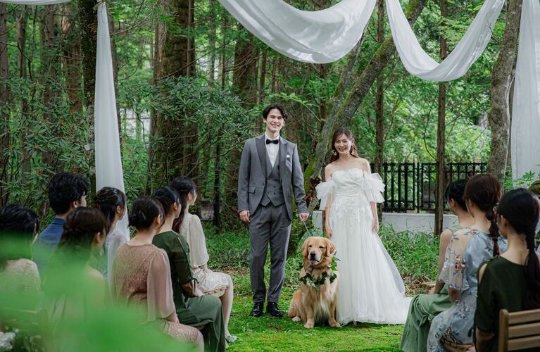 軽井沢の森で行う人前式。ウェディングドレスとタキシード姿の新郎新婦と、リングドッグの愛犬。ゲストに囲まれた、笑顔あふれるアネーリ軽井沢のガーデンウェディング。