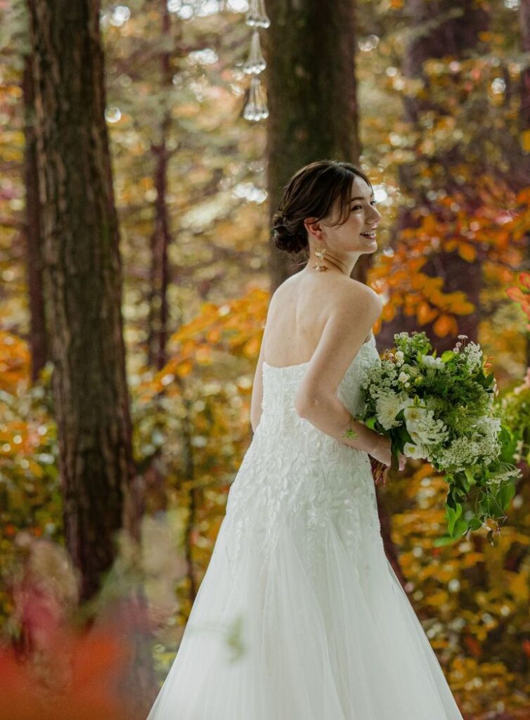 軽井沢の秋の結婚式。紅葉に囲まれた森の中で、純白のウェディングドレス姿で振り返る花嫁。アネーリ軽井沢で人気のロケーションフォト。