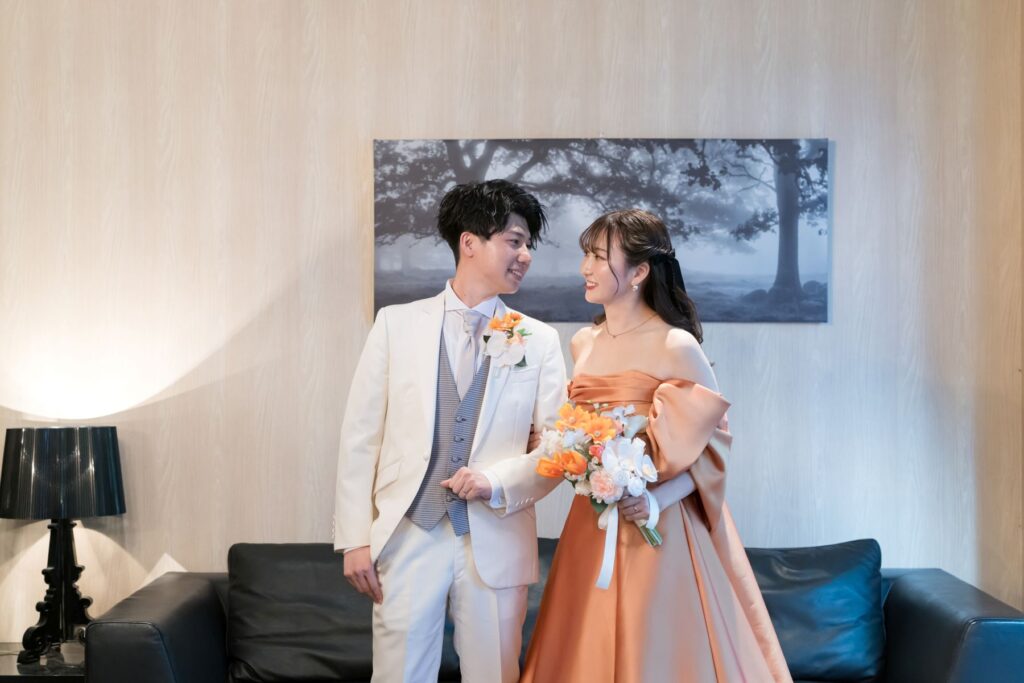 オレンジドレスと白タキシードが織りなす、スタイリッシュなお色直し。軽井沢の貸切邸宅で、ゲストとアットホームにくつろぐひとときを。アネーリ軽井沢が叶えるリゾートウエディング。