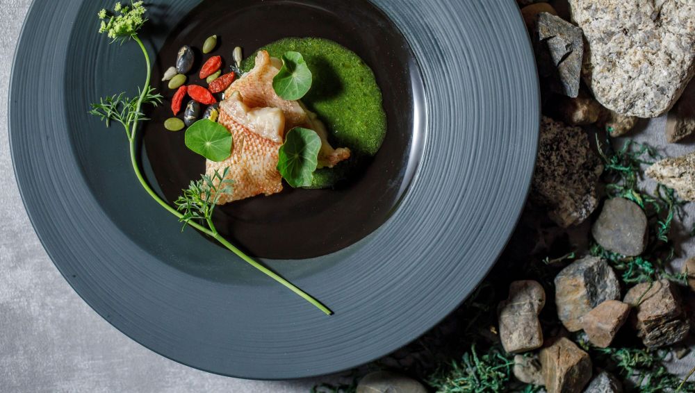 アネーリ軽井沢の信州フレンチ。皮目をパリッと香ばしくポワレした鮮魚のメイン料理を、濃厚な緑のハーブソースと木の実で飾った、芸術的な一皿。軽井沢での特別な美食体験。