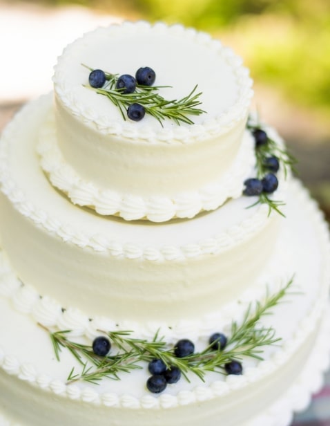 アネーリ軽井沢の軽井沢ウェディングに映えるオリジナルウェディングケーキ。シンプルな3段の生クリームケーキを、ブルーベリーとローズマリーでナチュラルに装飾。緑豊かな森でのケーキカットのひととき。