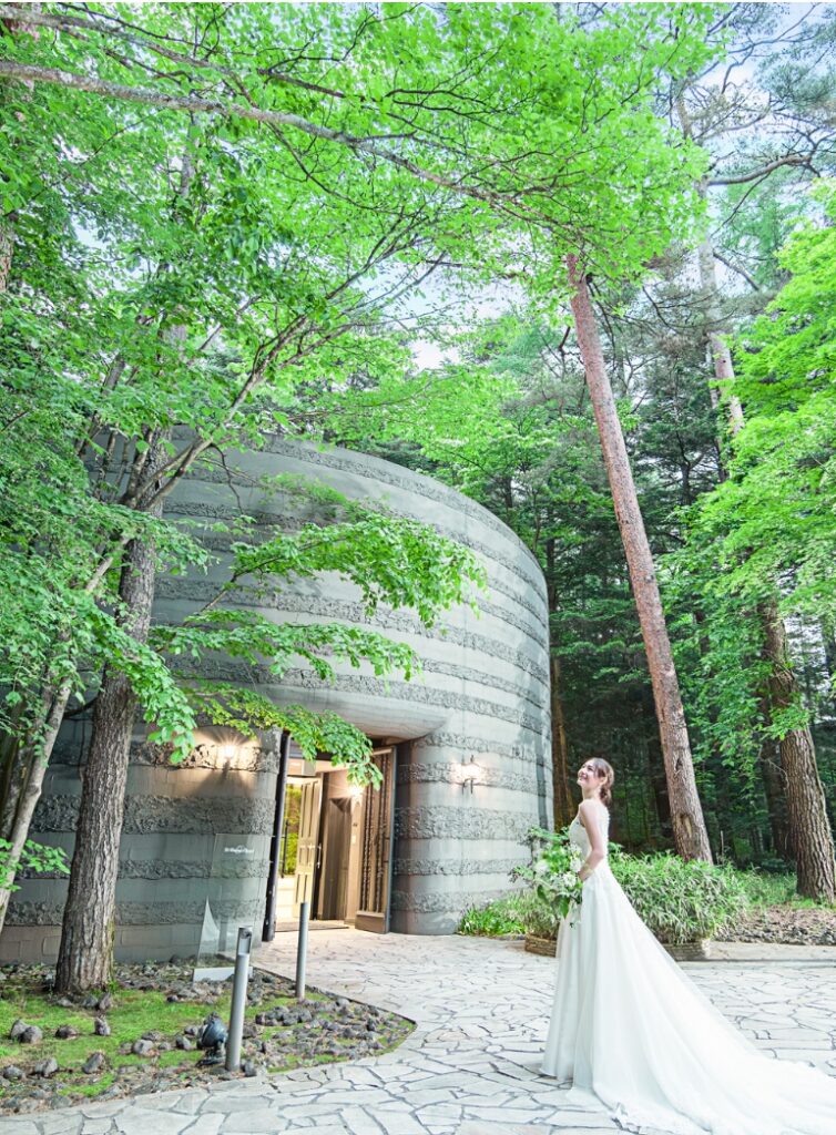 軽井沢の木立の中に佇む、アネーリ軽井沢のスタイリッシュな円形チャペル。石の壁と緑のコントラストが美しいリゾート挙式会場。洗練された雰囲気で愛を誓うウェディング。