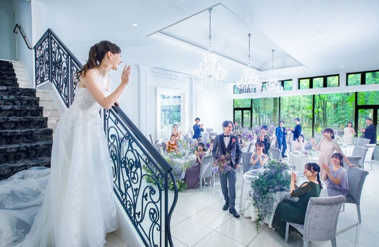 披露宴会場の階段からの再入場。新婦がゲストに手を振る、華やかで感動的な演出。軽井沢の森の光が差し込む、明るくエレガントなパーティ会場。
