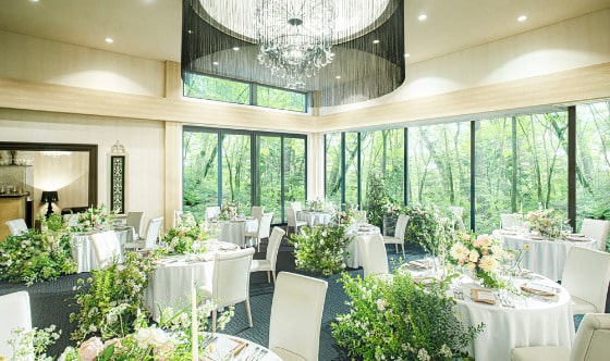 【ムーサイオン】軽井沢の森を一望する2面窓の披露宴会場。自然光と緑に囲まれた明るい空間で、ナチュラルな装花を施したアットホームなウェディングパーティ。