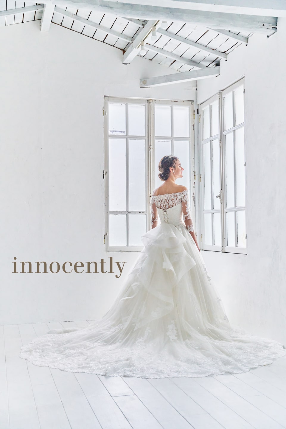 【innocently(イノセントリー)】のウェディングドレス。オフショルダーの長袖レースと幾重にも重なるフリルのトレーンが豪華なバックスタイル。アネーリ軽井沢の自然光が差し込むチャペルに映える一着。