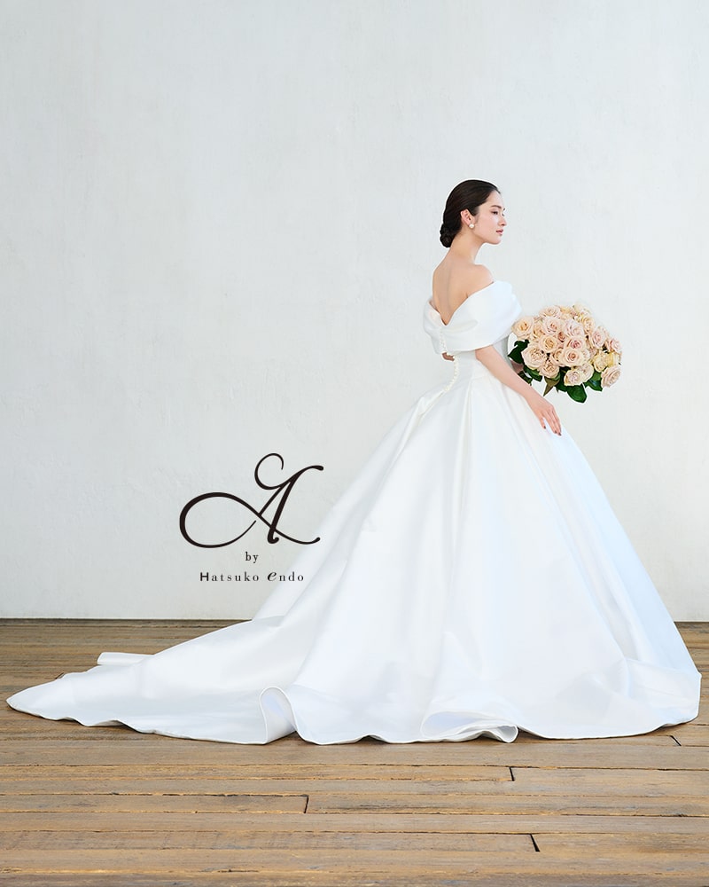 【Hatsuko Endo(ハツコエンドウ)】A by Hatsuko Endoのオフショルダー・ウェディングドレス。光沢のあるサテンのAラインで、ロングトレーンとくるみボタンがクラシカル。アネーリ軽井沢のチャペルに映える一着。