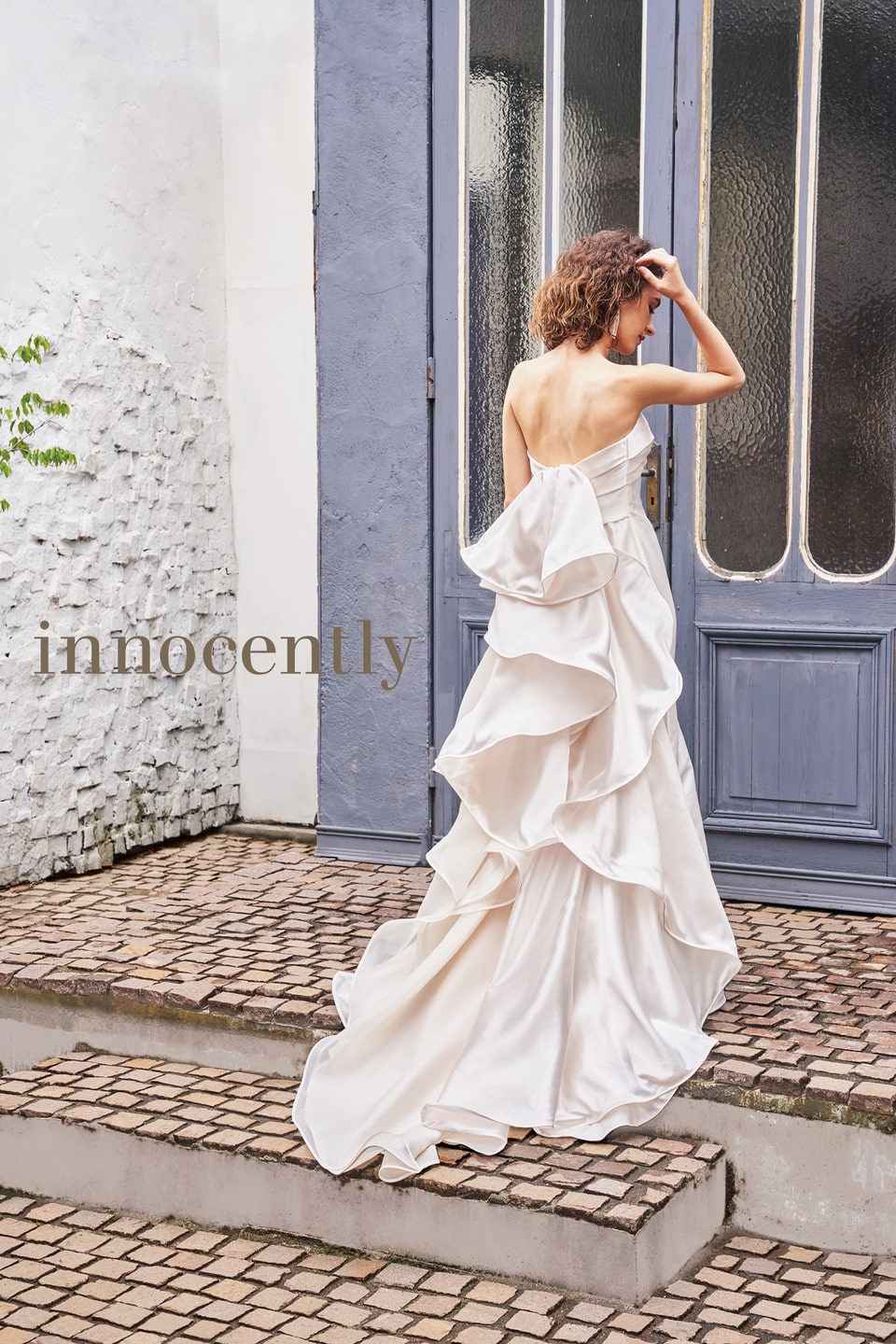 innocently(イノセントリー)のウェディングドレス。オフホワイトの光沢サテン生地で、大きなバックリボンと何層ものティアードフリルが優雅なバックスタイル。軽井沢のフォトに映える優美な一着。