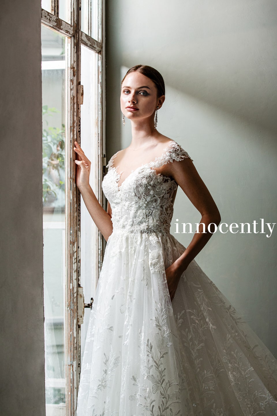 innocently(イノセントリー)の刺繍レースウェディングドレス。AラインとVネック、オフショルダーのキャップスリーブが華奢な印象。アネーリ軽井沢の窓際で、ナチュラルで上品な花嫁姿を演出。