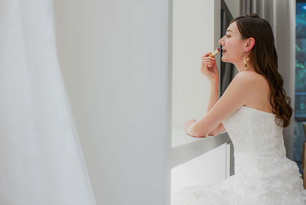 アネーリ軽井沢のブライズルームでのワンシーン。ウェディングドレス姿の花嫁様が、結婚式直前にメイク（リップ）を直している様子。明るい自然光が入るブライズルームで、軽井沢ウェディングの挙式・披露宴に向けて準備中の花嫁の様子を撮影。お洒落でリアルなオフショット。