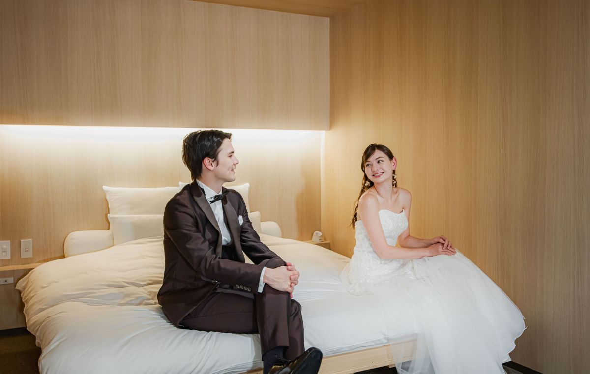 【アネーリ軽井沢の宿泊】軽井沢ウェディングで利用できるスイートルームで、ウェディングドレスとタキシード姿の新郎新婦。結婚式当日のリラックスしたオフショット撮影や、前撮りでの利用に人気。ナチュラルで温かみのある客室で、軽井沢リゾートウェディングの思い出を残すお洒落な写真。