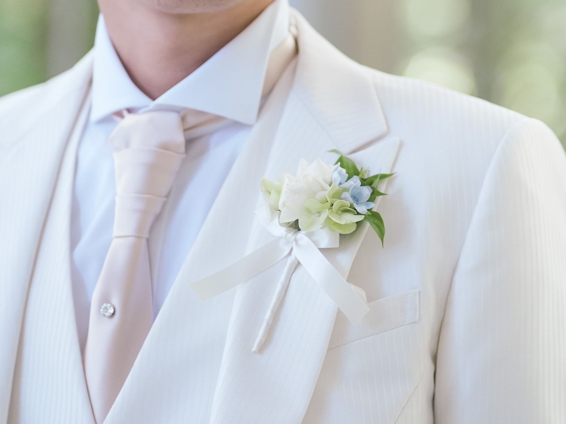 新郎のタキシードスタイル。優しいオフホワイトのタキシードに淡いピンクのタイが洗練された印象に。上品なブートニアを添えて、軽井沢の自然に映える華やかな装いを。