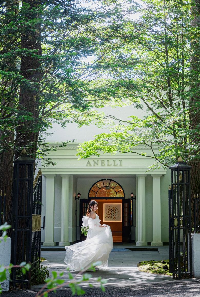 アネーリ軽井沢の緑豊かなエントランス前で、ウェディングドレス姿の美しい新婦が軽やかに歩く前撮り・フォトウェディングのワンシーン