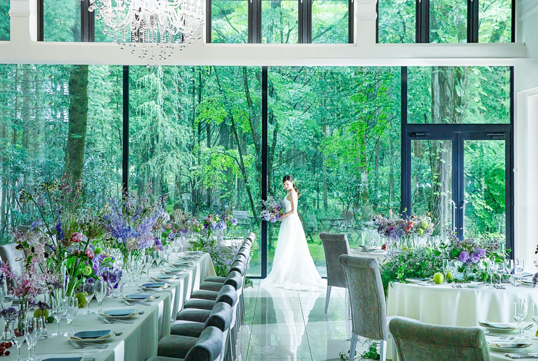 アネーリ軽井沢のガーデンビューの披露宴会場。ガラス一面に広がる森の緑と、紫の装花が美しく調和した空間。自然光に満ちた上質なウェディングパーティ。
