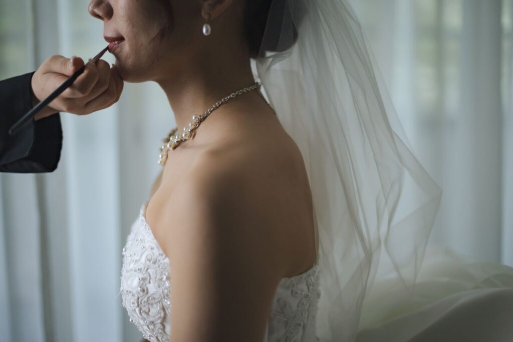 柔らかな光に包まれた花嫁のリップメイクシーン。挙式前の特別な支度時間を美しく描きます。花嫁の表情を引き立てる丁寧なヘアメイクは、写真映えと当日の安心感を両立する人気ポイントです。