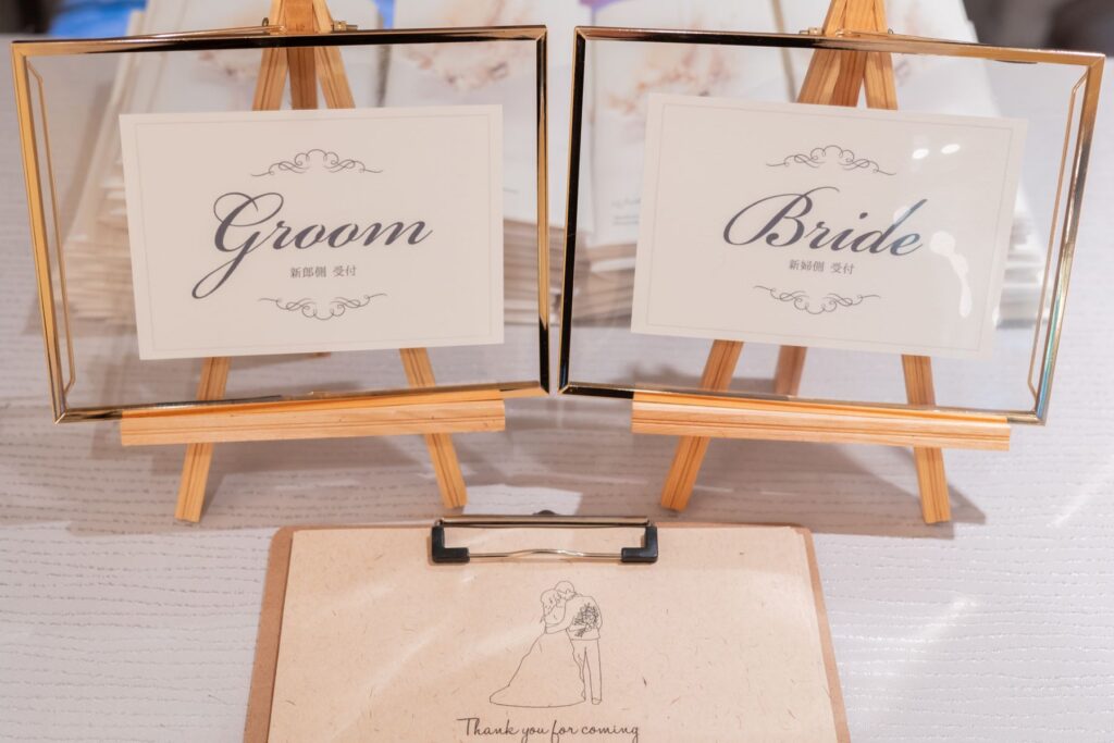 受付スペースに並ぶ「Groom」「Bride」のサインが、ゲストを上品にお迎えするウェディングシーン。シンプルながら洗練されたデザインは、会場全体の統一感を高め、おふたりらしいおもてなしを演出します。写真映えも叶う人気のウェルカムアイテムです。