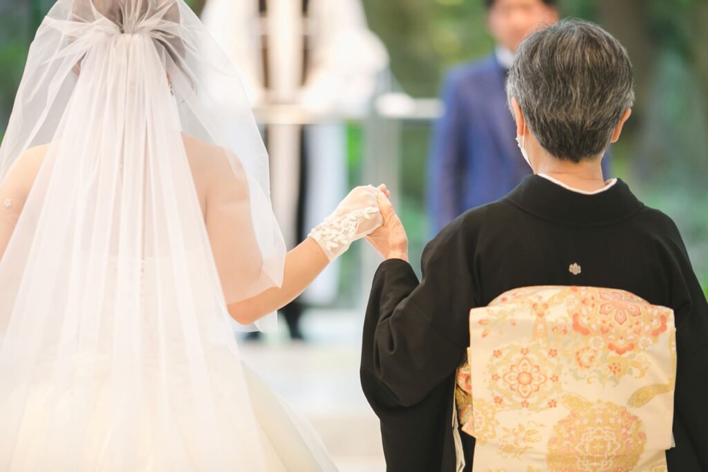 やわらかな光に包まれ、母と手を取り合いながら歩む感動のワンシーン。和装とドレスが織りなす美しい瞬間は、家族の絆や感謝の想いを伝える特別なセレモニーとして、多くの花嫁様に選ばれています。心に残る挙式演出の一例です。