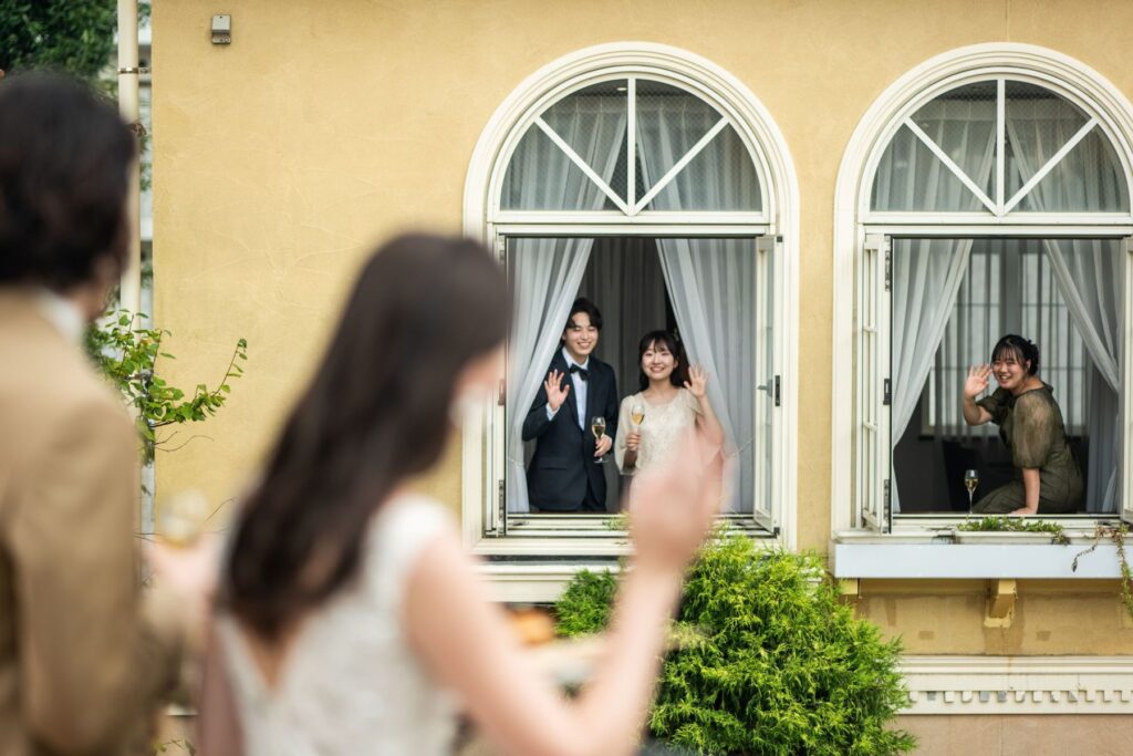 南欧風の窓から手を振る新郎新婦。温かく感動的なお見送りの瞬間