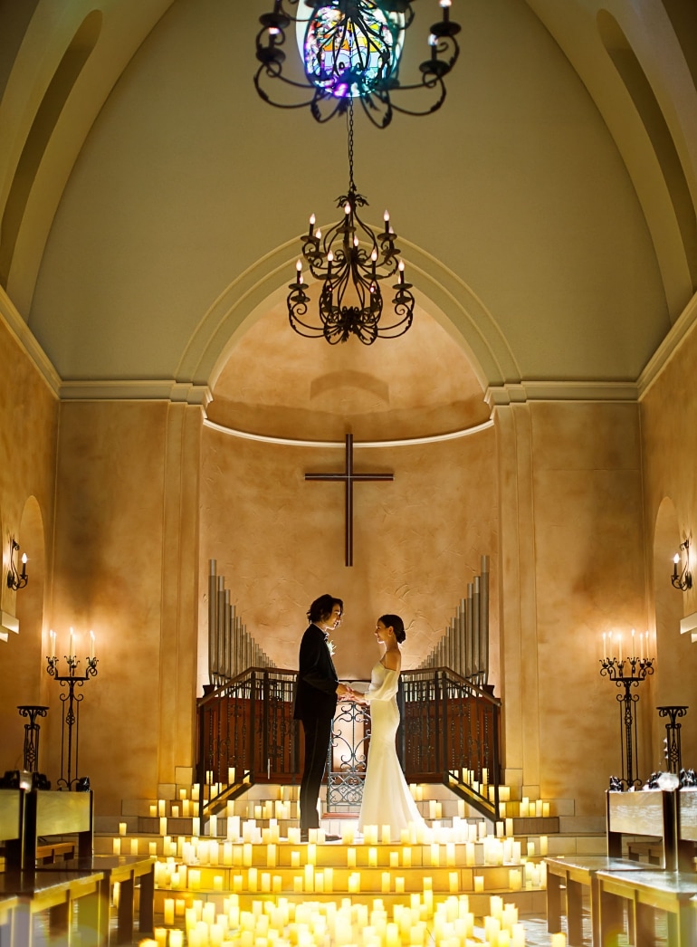 さいたま市の結婚式場アネーリ大宮。無数のキャンドルが輝く幻想的な大聖堂で、手を取り見つめ合う新郎新婦。ロマンティックなナイトウェディングの挙式風景