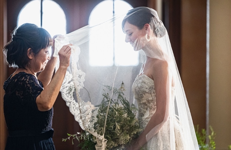 さいたま市の結婚式場アネーリ大宮。柔らかな光の中、母から花嫁へ最後の身支度となるベールダウン。親子の絆と感謝が溢れる感動的なウェディングフォト。
