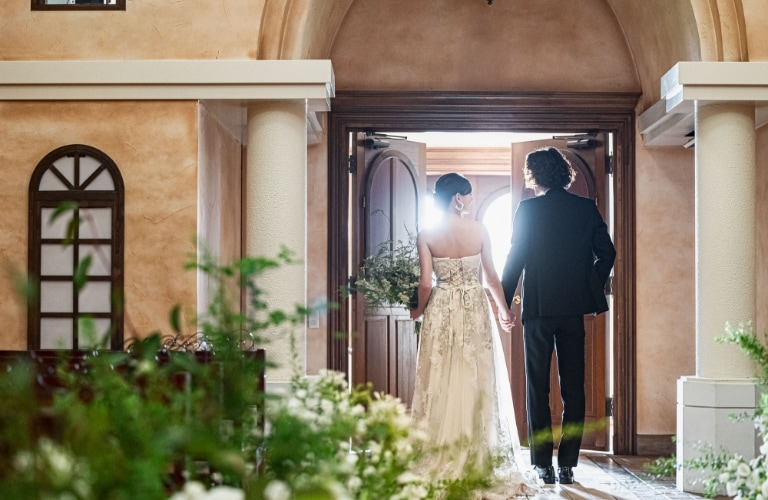さいたま市の結婚式場アネーリ大宮。大聖堂の扉が開き、光の中へ歩み出す新郎新婦の後ろ姿。ふたりの輝かしい未来を象徴する、感動的なウェディングフォト。