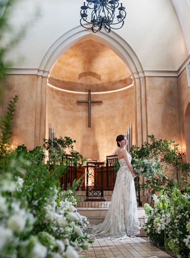 さいたま市の結婚式場アネーリ大宮。緑と花々が彩る森のような大聖堂。十字架を背にウェディングドレス姿の花嫁が佇む、幻想的で神聖な一枚。