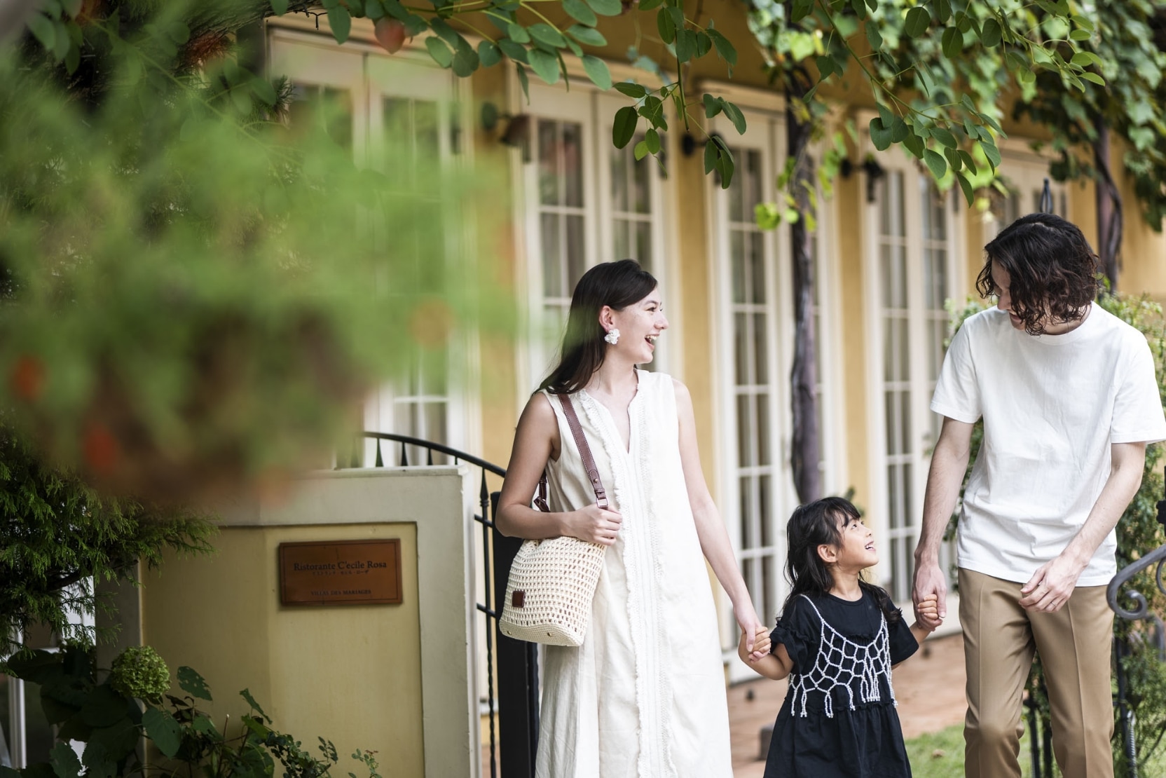 さいたま市の結婚式場アネーリ大宮「ノス・ド・フロマン」。緑のガーデンで手を繋ぎ歩く家族3人。記念日に再訪し、思い出を重ねる幸せなひととき。