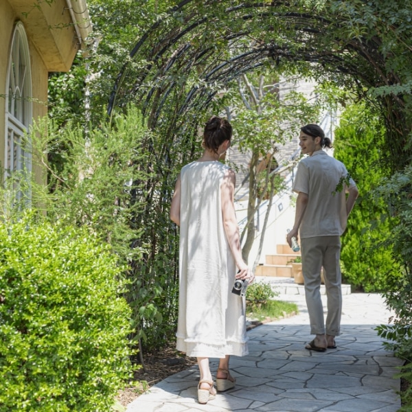 さいたま市の結婚式場アネーリ大宮「ノス・ド・フロマン」。緑のアーチの下、カメラを片手に思い出を巡る二人。記念日に再訪し、ゆったりと過ごす大人のデート。