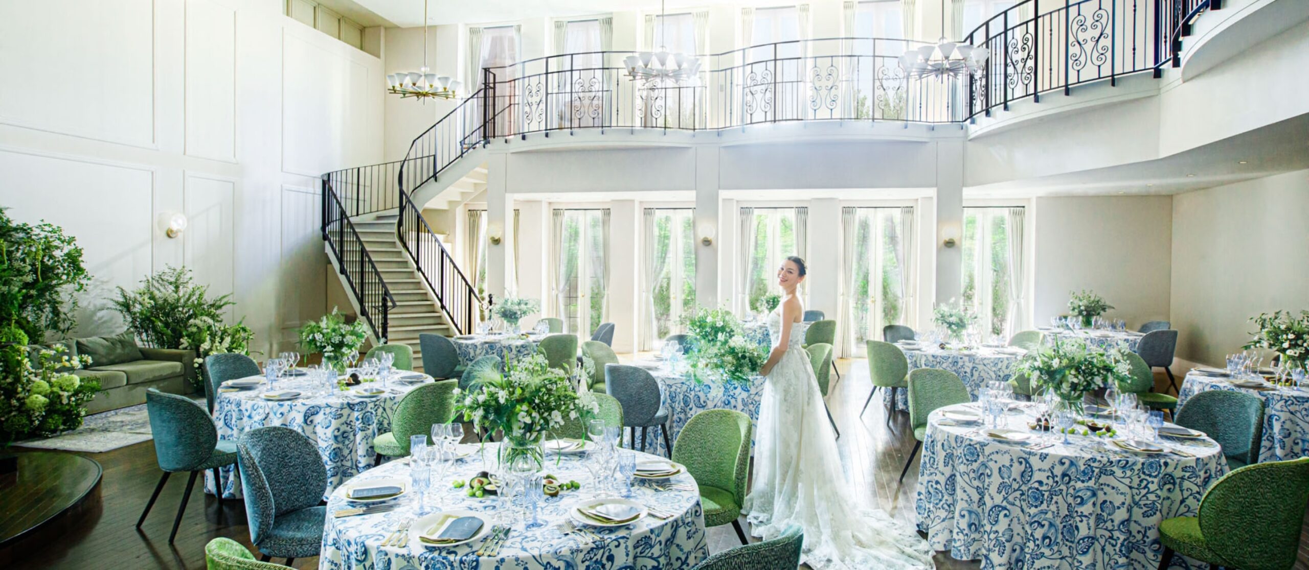 さいたま市の結婚式場アネーリ大宮。自然光注ぐ白亜の会場に、憧れの大階段と爽やかな青と緑のコーディネートが映える。