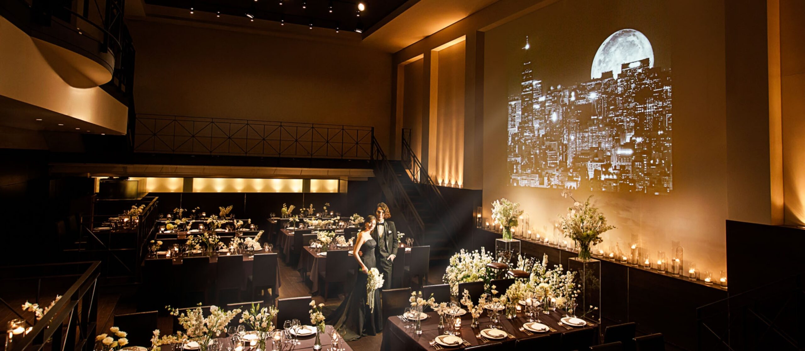 さいたま市の結婚式場アネーリ大宮。イルミネーションが輝くバルコニーで乾杯する新郎新婦。ゲストを見下ろし、ロマンチックなひとときを過ごす。