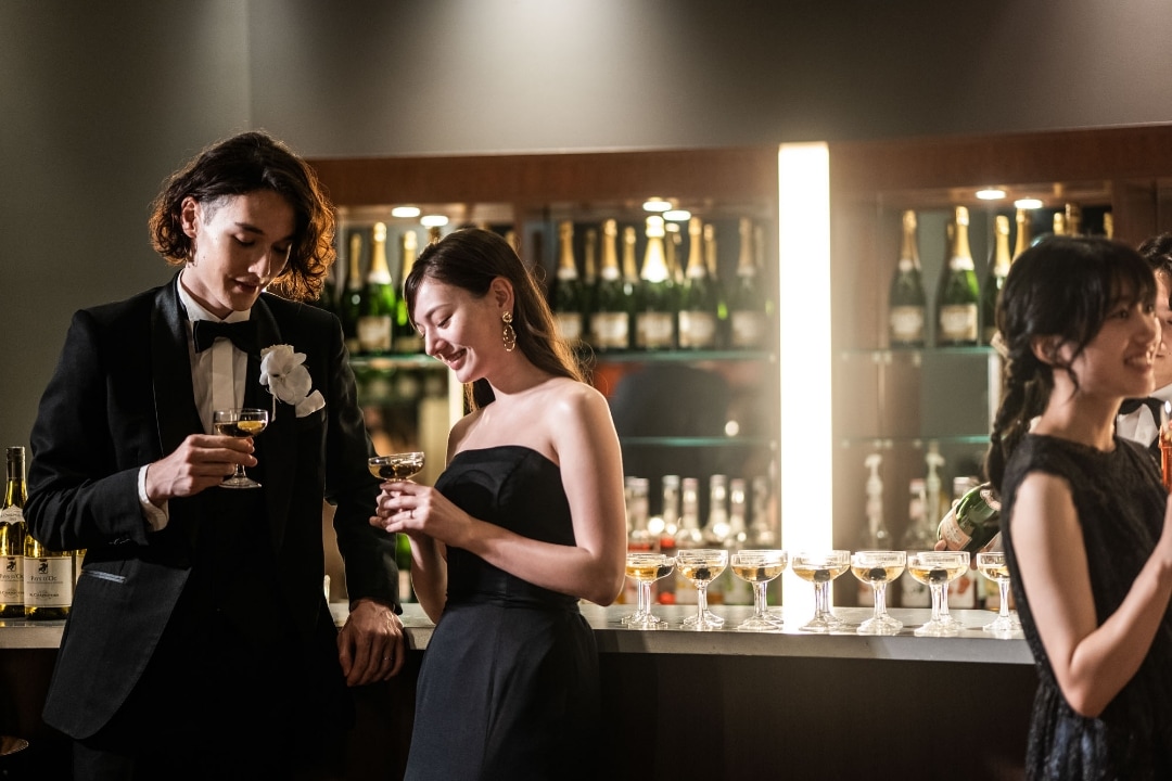 さいたま市の結婚式場アネーリ大宮。バーカウンターでカクテルを手に語らう新郎新婦。ブラックドレスが映える、シックで大人なナイトウェディング。