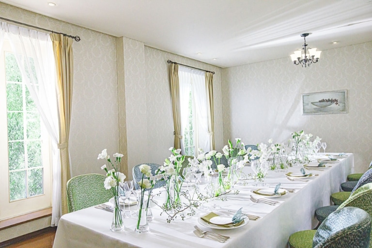 さいたま市の結婚式場アネーリ大宮。自然光が注ぐ少人数専用会場。白と緑の装花が彩る長テーブルで、家族と過ごすアットホームな会食ウェディング。