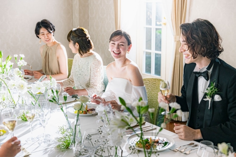 さいたま市の結婚式場アネーリ大宮。少人数の食事会ウェディングで、ゲストとテーブルを囲み談笑する新郎新婦。笑顔が絶えないアットホームなパーティ。