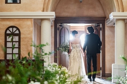さいたま市の結婚式場アネーリ大宮。大聖堂の重厚な扉が開き、光に包まれて歩み出す新郎新婦の後ろ姿。輝かしい未来を予感させる感動的なワンシーン