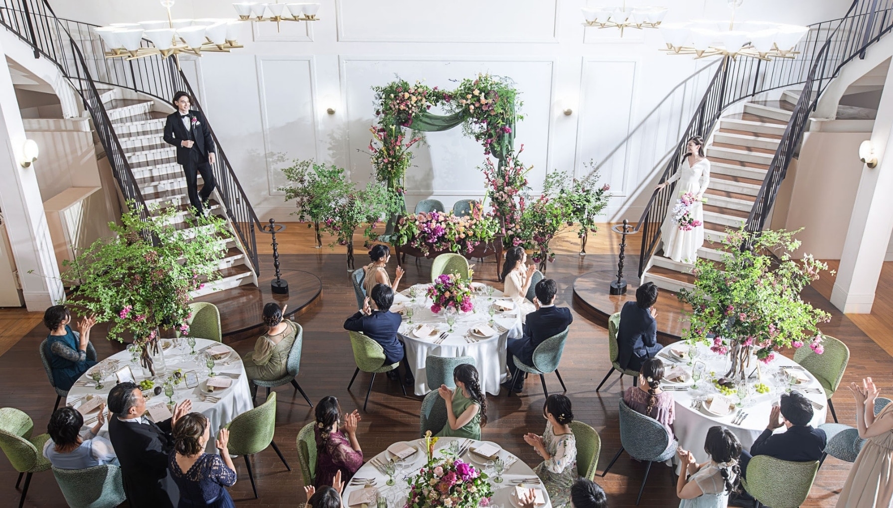 さいたま市の結婚式場アネーリ大宮。自然光溢れる白亜の会場で、左右の大階段から新郎新婦が登場するドラマチックな演出。ゲストの歓声に包まれる披露宴風景。
