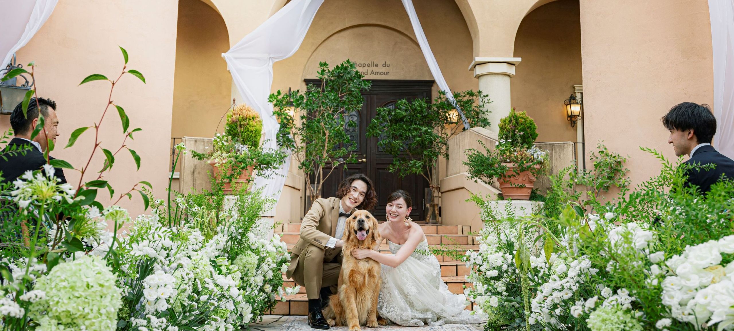 さいたま市の結婚式場アネーリ大宮。緑豊かなガーデンで、愛犬と一緒に笑顔を見せる新郎新婦。大切なペットも家族として参加できるアットホームな挙式。