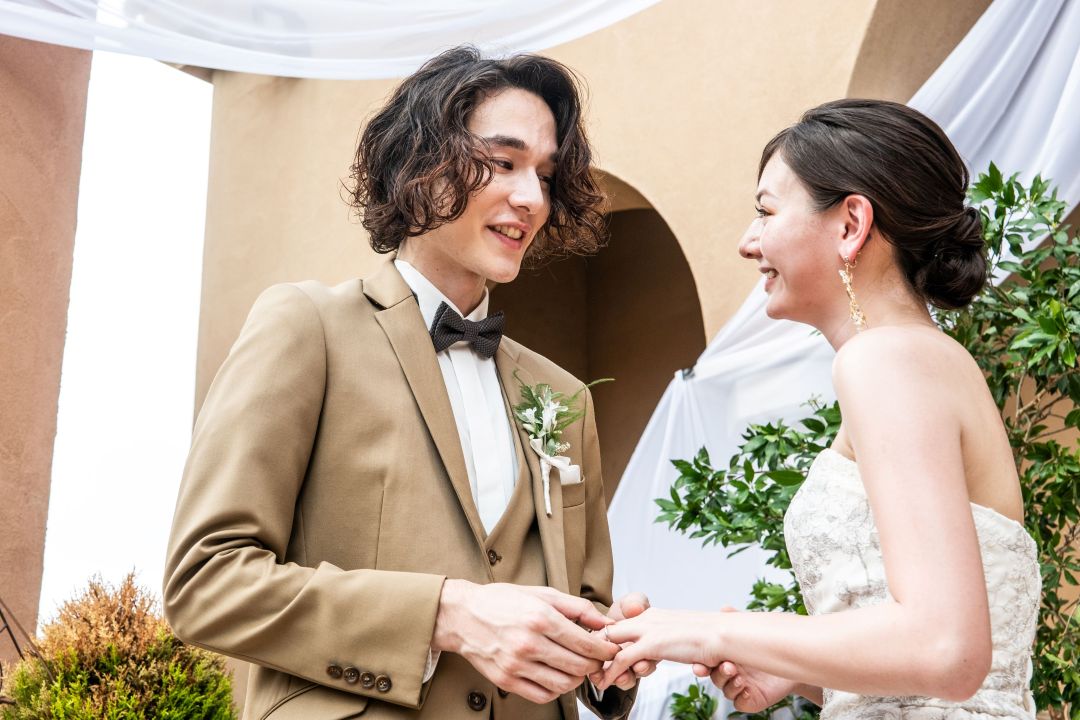 さいたま市の結婚式場アネーリ大宮。ガーデン挙式で、永遠の愛を誓う指輪交換。笑顔で見つめ合う新郎新婦の親密で感動的なワンシーン。