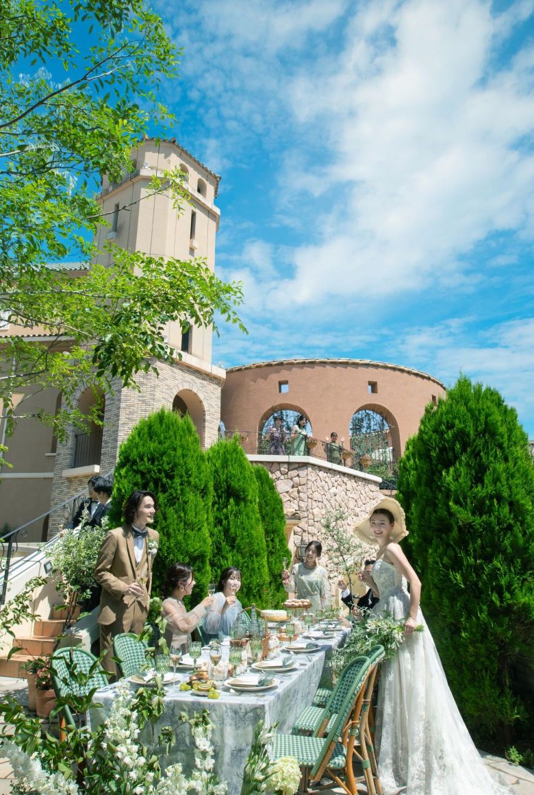 さいたま市の結婚式場アネーリ大宮。青空の下、緑溢れるヨーロッパ風の中庭で、ゲストと会話や食事を楽しむ開放的なガーデンパーティの風景。
