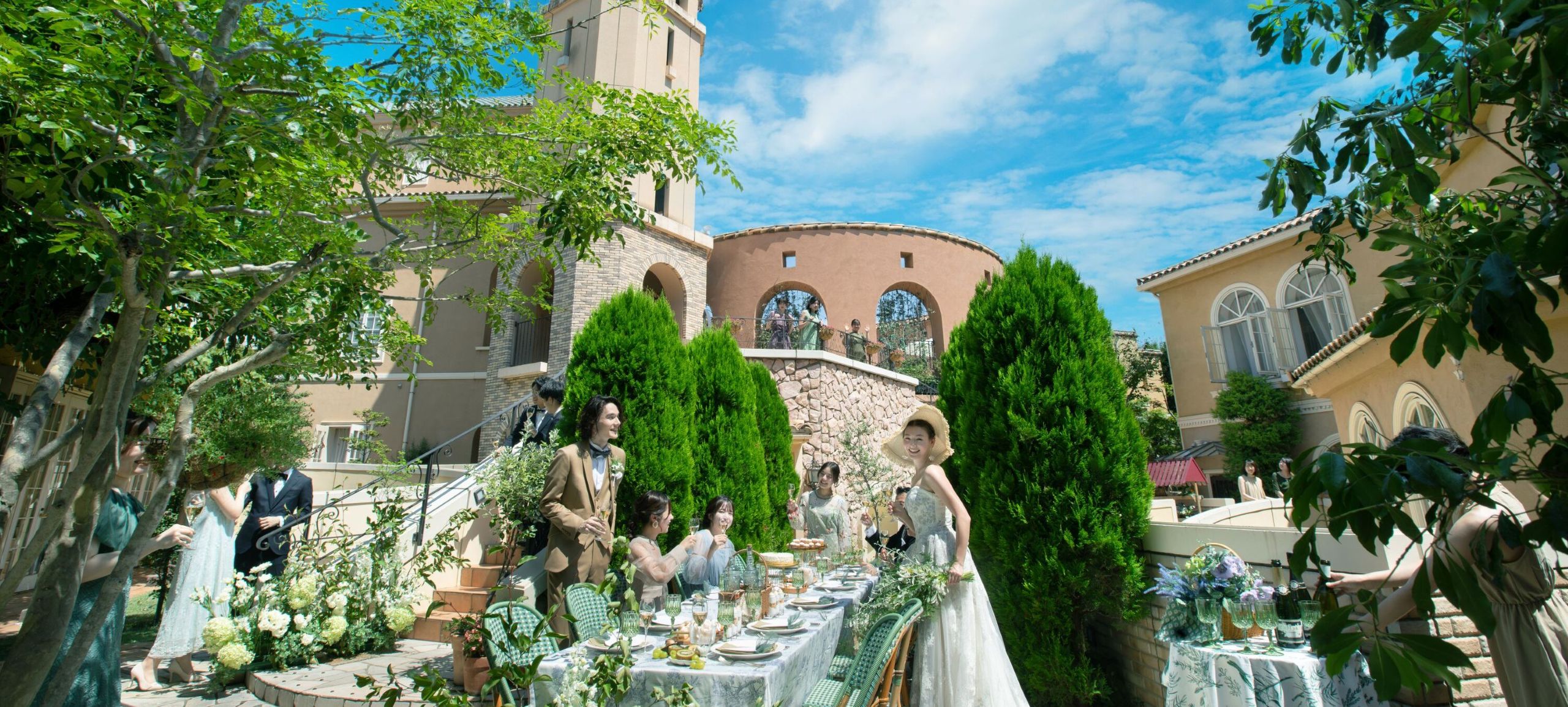 さいたま市の結婚式場アネーリ大宮。青空の下、緑溢れるヨーロッパ風の中庭で、ゲストと会話や食事を楽しむ開放的なガーデンパーティの風景。