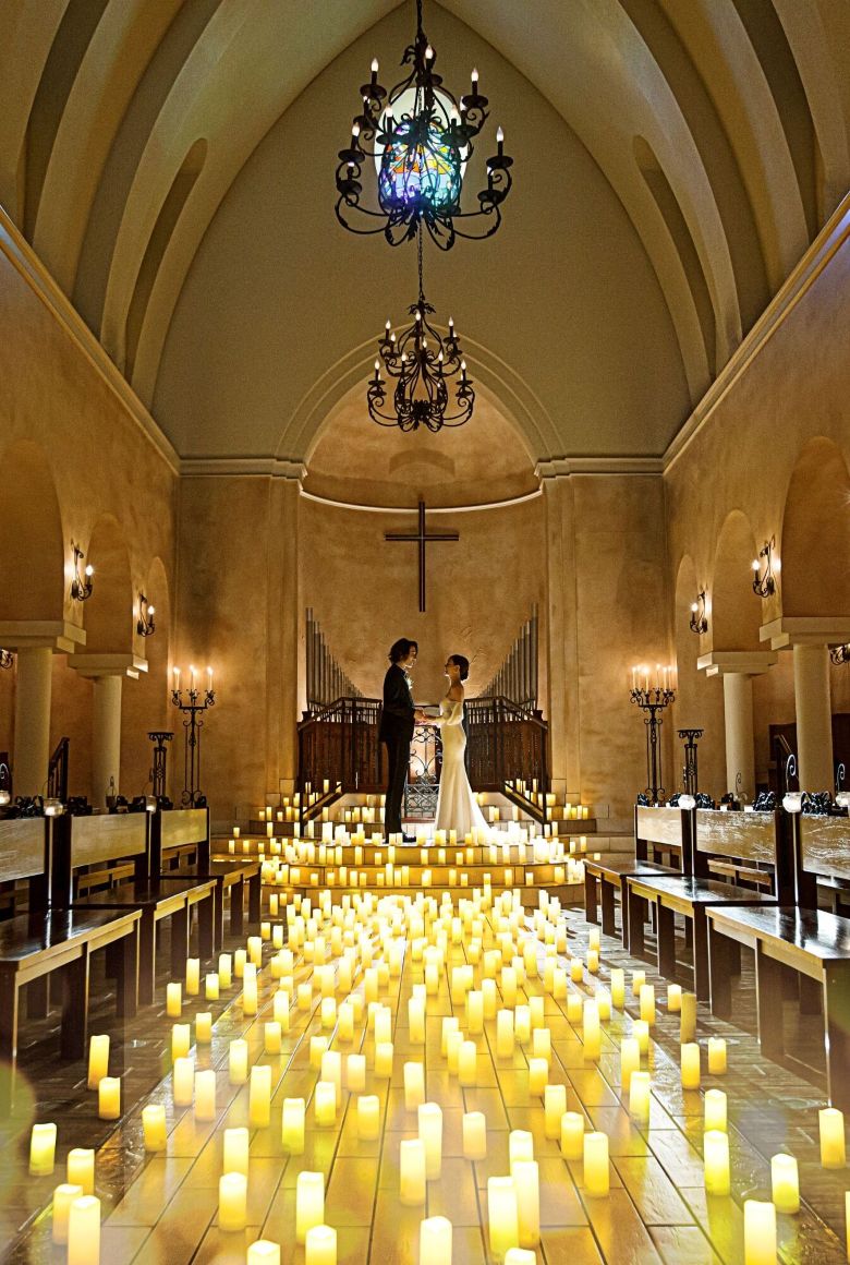 さいたま市の結婚式場アネーリ大宮。無数のキャンドルが輝く幻想的な大聖堂で、手を取り合う新郎新婦。ロマンティックなナイトウェディングの挙式風景。