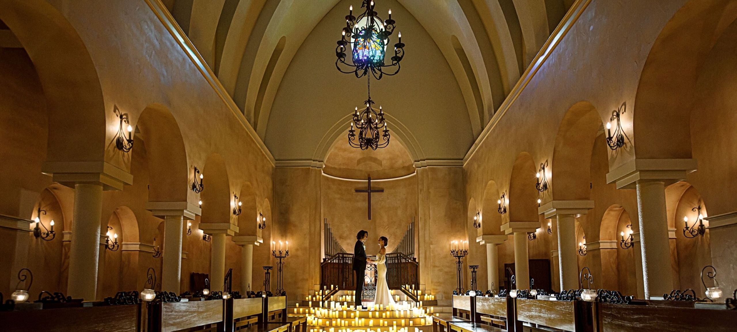 さいたま市の結婚式場アネーリ大宮。無数のキャンドルが輝く幻想的な大聖堂で、手を取り合う新郎新婦。ロマンティックなナイトウェディングの挙式風景。
