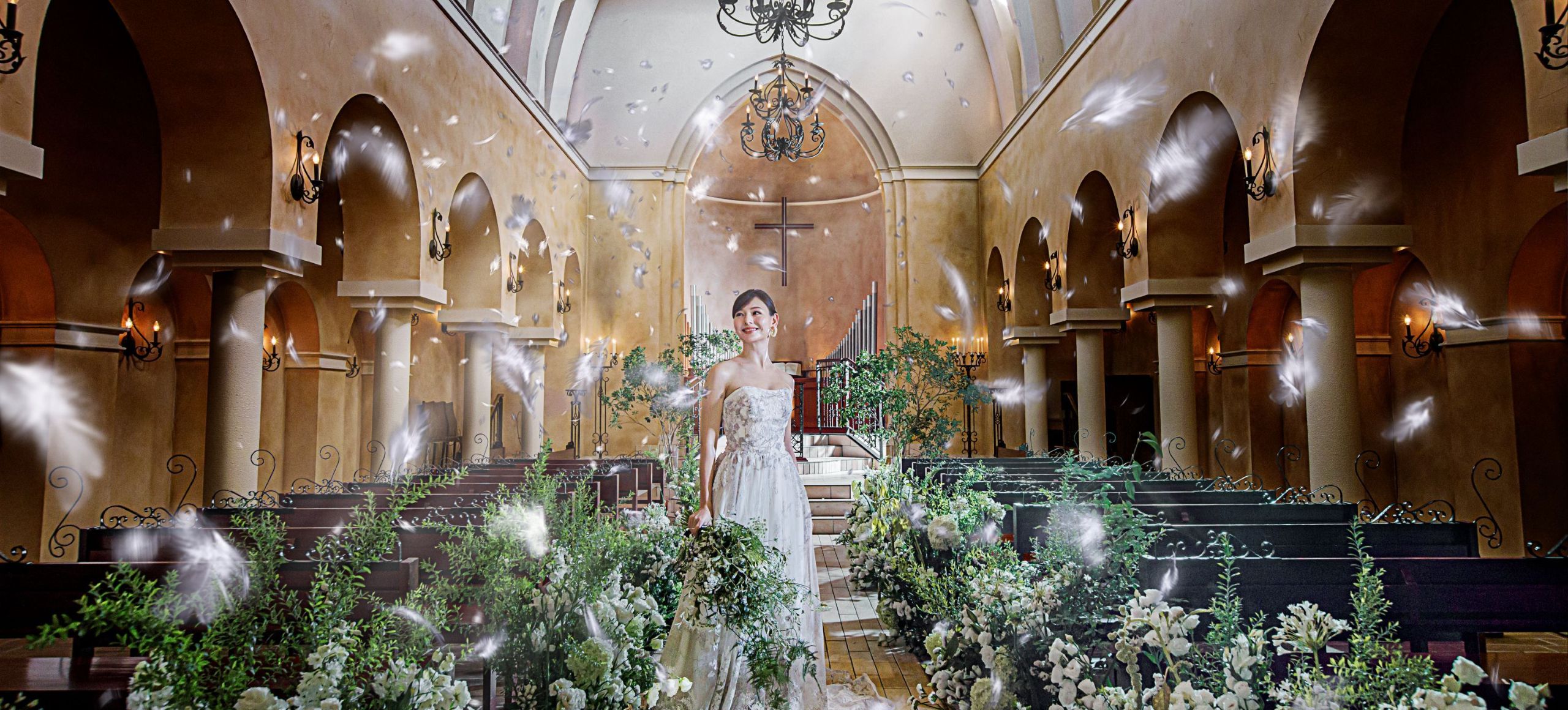 さいたま市の結婚式場アネーリ大宮。緑豊かな大聖堂に、天使の羽が舞い降りるフェザーシャワー。幻想的な光と祝福に包まれ、笑顔で佇む花嫁。