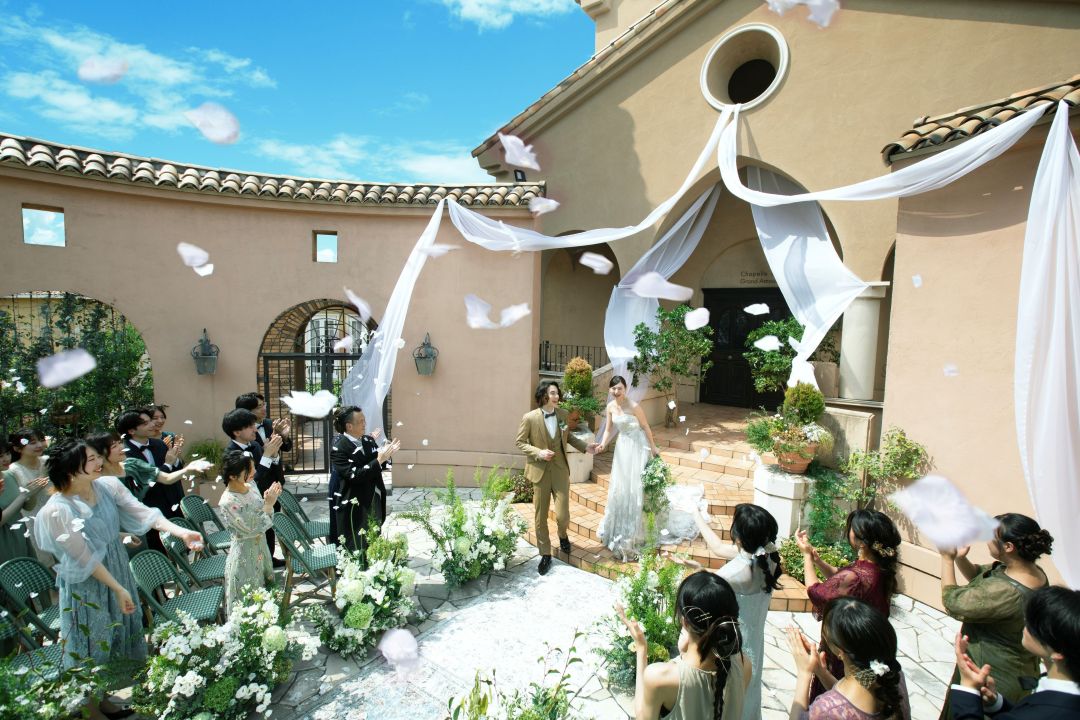 さいたま市の結婚式場アネーリ大宮。青空の下、ガーデン挙式でフラワーシャワーの祝福を浴びる新郎新婦。ゲストの笑顔と拍手に包まれた開放的なアフターセレモニー。