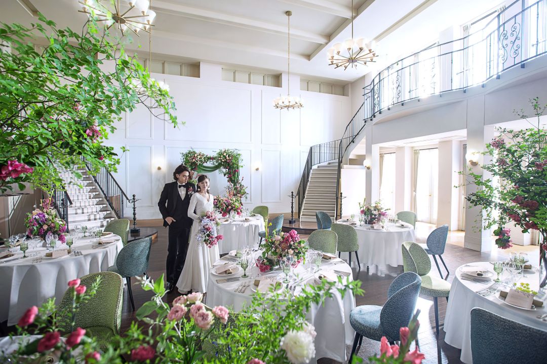 さいたま市の結婚式場アネーリ大宮。白亜の会場に映えるピンクの装飾。アーチ状の装花と大階段が特徴の、ロマンティックで華やかな披露宴風景